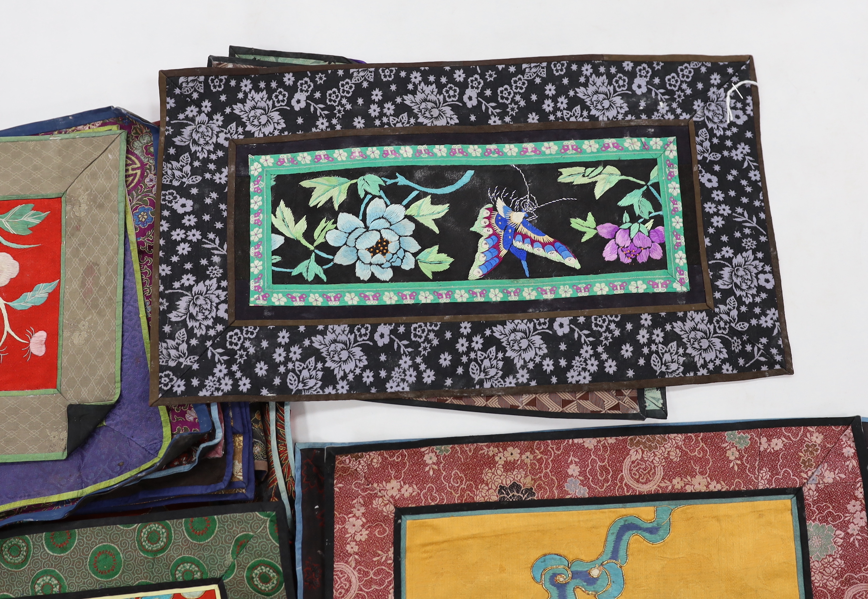 Twenty six assorted Chinese polychrome silk embroidered mats with silk damask borders of varying sizes